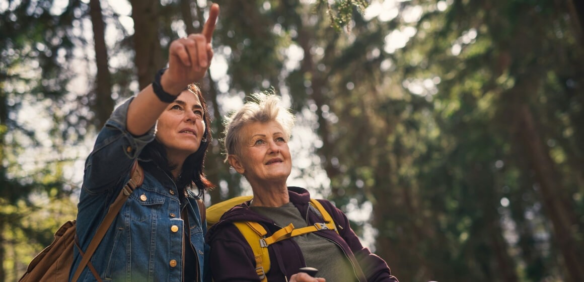Deux femmes en randonnée dans une forêt, la plus jeune pointe vers le haut tandis que l'aînée regarde avec un sac à dos