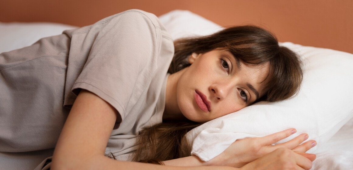 Jeune femme allongée dans un lit, la tête sur un oreiller, l'air fatiguée
