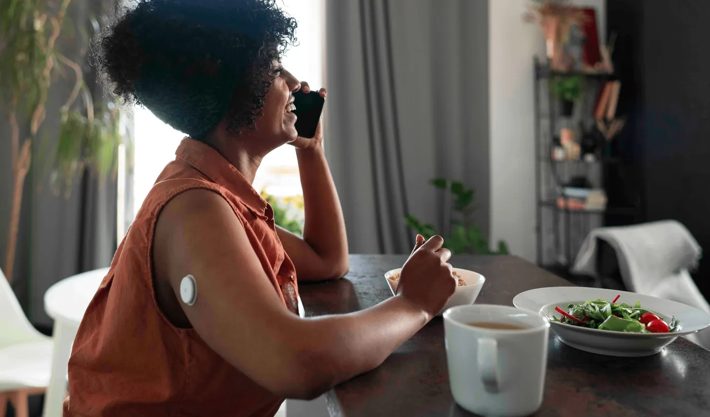 Femme avec un capteur de glycémie au bras mangeant un repas tout en téléphonant